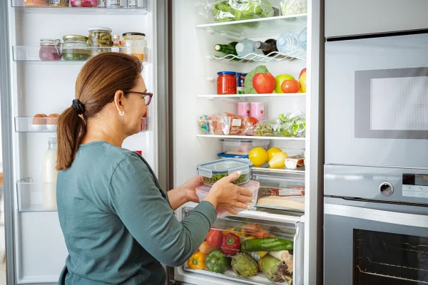 Mulher guarda recipientes com alimentos na geladeira. Metrópoles