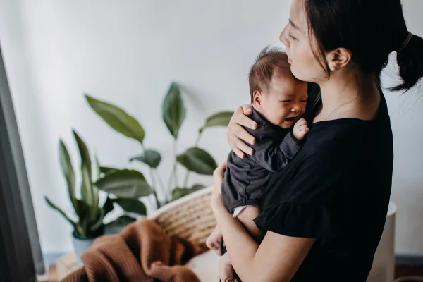 Uma jovem mãe asiática amorosa carregando sua filha recém-nascida nos braços, consolando e confortando seu bebê que chora. Fome e desconforto. Amor e cuidado. Conceito de maternidade e parentalidade. Metrópoles