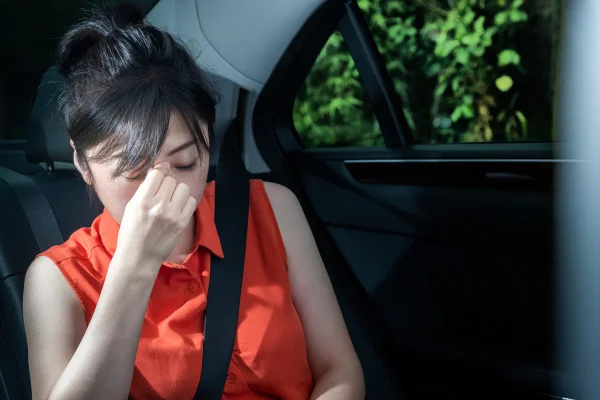 Mulher jovem asiática com mão na cabeça sentada em banco de trás do carro - Metrópoles