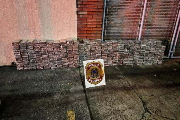 Imagens coloridas mostram centenas de tabletes de cocaína empilhados e um cartaz com símbolo da Polícia Federal à frente