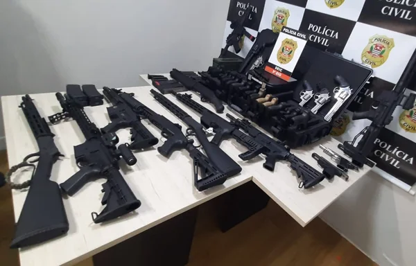 Imagem colorida de cerca de dez fuzis pretos colocados sobre uma mesa branca - Metrópoles