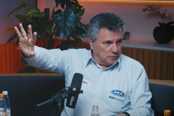 Homem branco com cabelo grisalho estica braço direito; ele fala ao microfone - Metrópoles