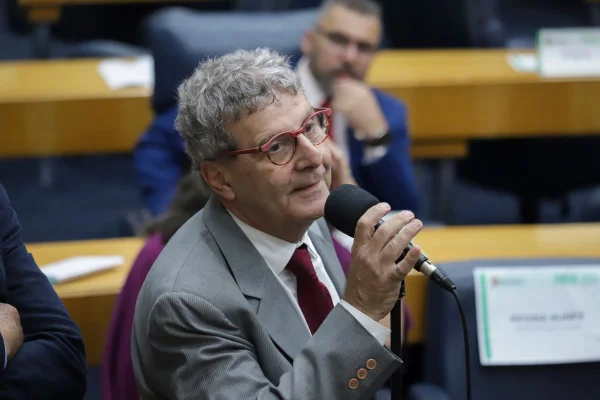 IMAGEM colorida mostra vereador nabil bonduki. ele usa terno cinza, gravata vermelha, e óculos vermelhos. tem cabelo grisalho e pele branca