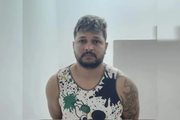 Imagem de um homem com barba, cabelo loiro, vestindo camiseta colorida. Ele tem tatuagem no braço esquerdo