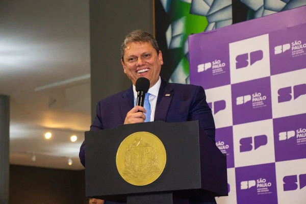 Imagem colorida mostra o governador Tarcísio de Freitas, de terno e gravata azul em um pulpito, segurando microfone, enquanto sorri - Metrópoles