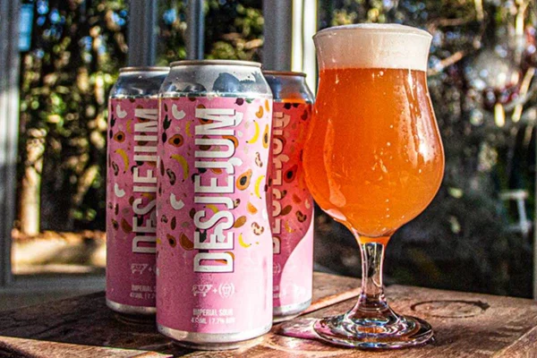 Três latas de cerveja ao lado de copo com cerveja