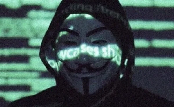 Em vídeo divulgado pelos Anonymous, pessoa usa a máscara do grupo, de capuz, e em seu rosto e no fundo são refletidas palavras em verde - Metrópoles
