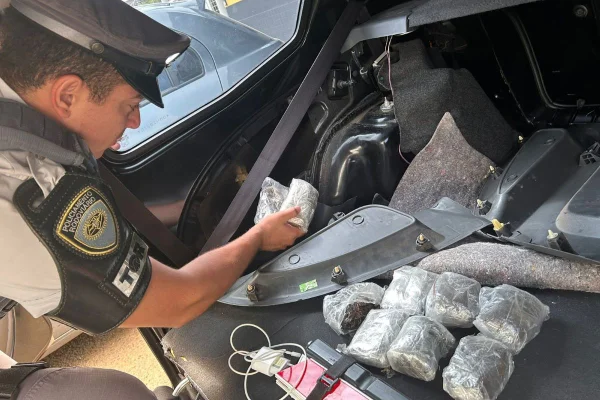 Imagem colorida mostra policial recolhendo tijolos de haxixe em carro - Metrópoles