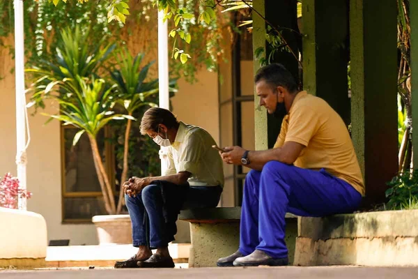 Dois homens sentados na guia, em Goiânia, um de máscara e outro com máscara abaixada