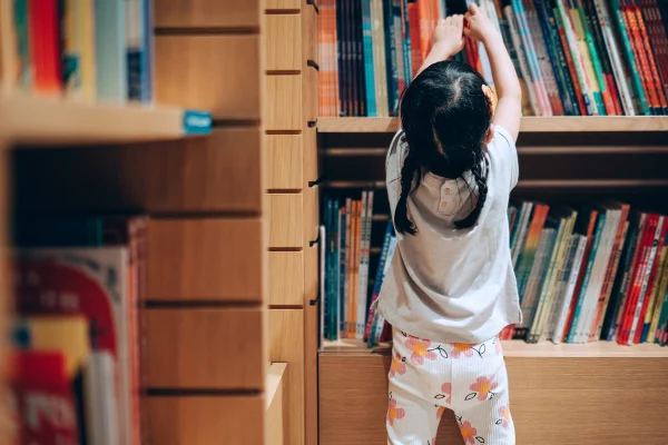 Imagem colorida de uma criança pequena escolhendo livros de uma estante