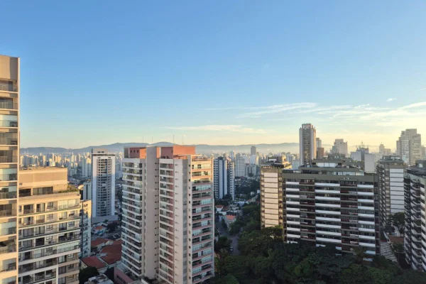Imagem colorida mostra horizonte com muitos prédios, céu azul e sol - Metrópoles