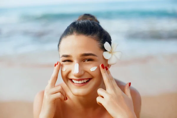 mulher com uma flor no cabelo passando protetor solar