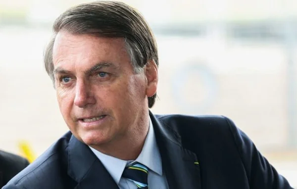 Bolsonaro cumprimenta turistas na frente do Alvorada. Ele usa terno e gravata e olha para o lado - Metrópoles