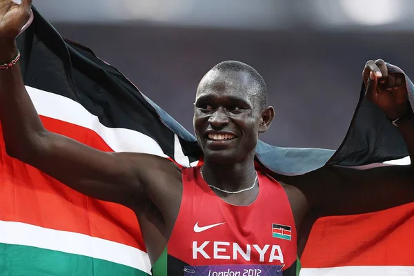 David Lekuta Rudisha, um homem negro sorrindo e com os braços abertos enquanto segura uma bandeira do Quênia