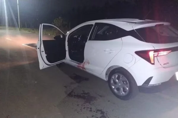 Imagem colorida de carro branco com manchas de sangue e porta aberta. Metrópoles
