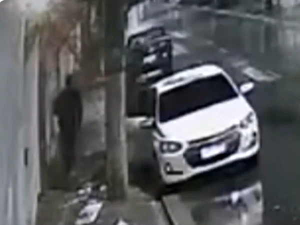 Imagem em preto e branco mostra homem saindo de carro em direção a portão de casa