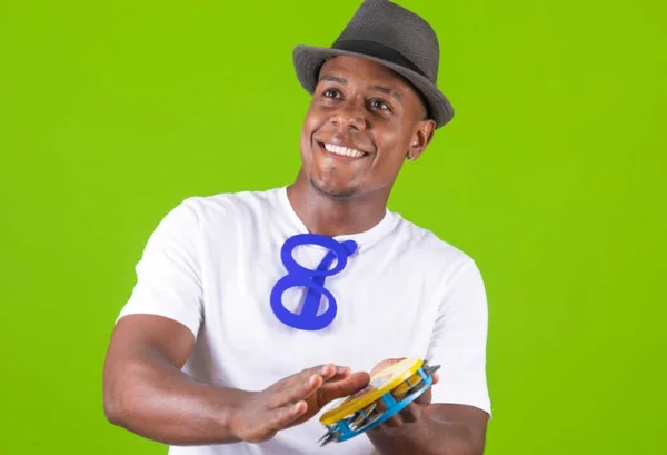 Homem com blusa branca com pandero na mão e fundo verde