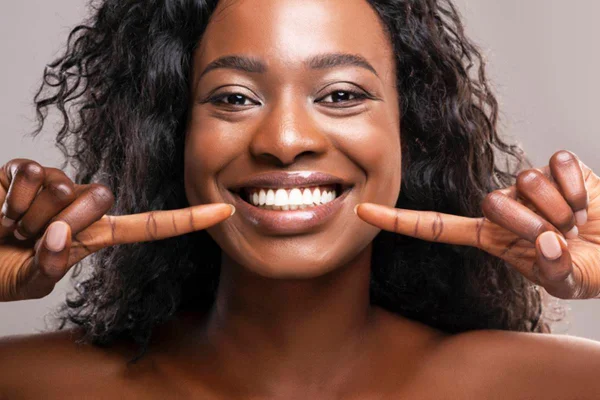 Mulher sorridente apontando com as duas mãos para os próprios dentes