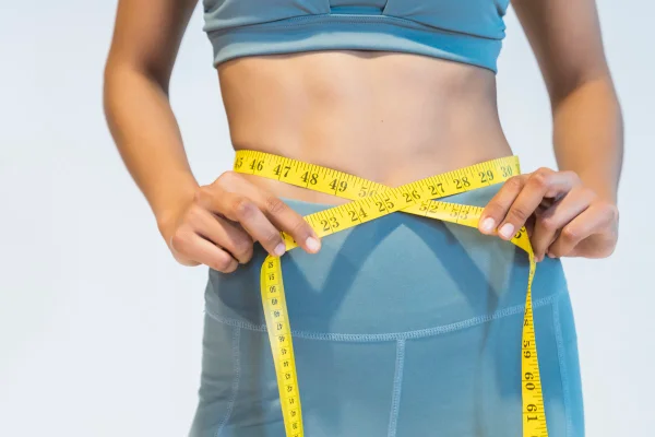 Foto colorida de mulher com fita métrica amarela na cintura - Metrópoles