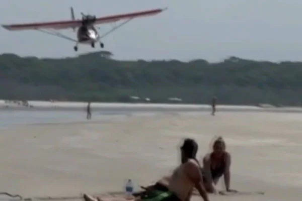 Imagem colorida de aeronave fazendo voo rasante perto de banhistas na praia