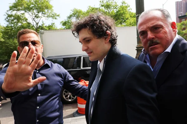Sam Bankman-Fried, fundador da FTX, chegando para prestar depoimento em julgamento. Ele é escoltado por seguranças e veste um terno azul escuro com gravata e camisa branca - Metrópoles