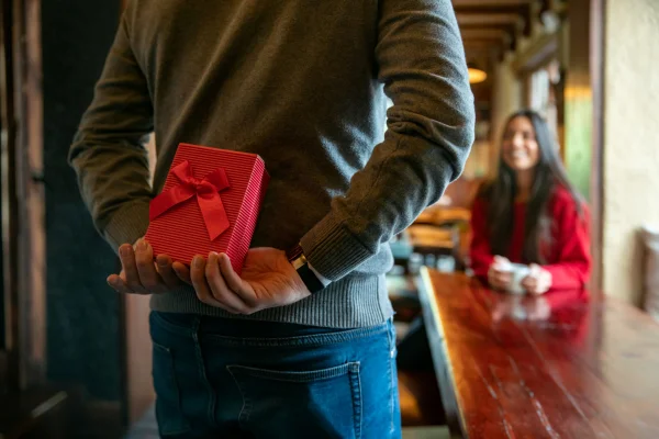 Homem latino-americano surpreende mulher com um presente enquanto comemora o Dia dos Namorados em um restaurante
