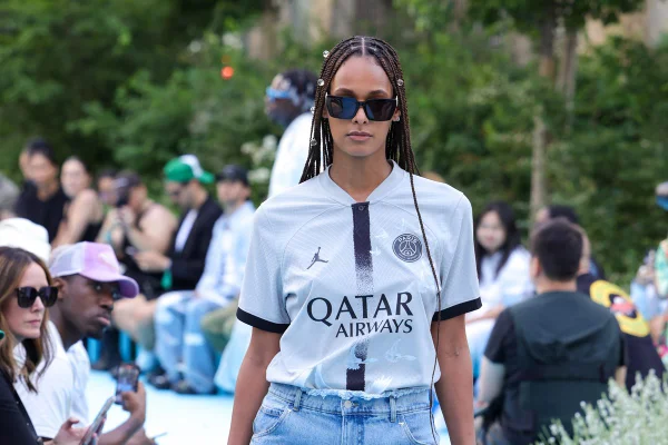 Modelo negra com tranças desfila usando a camisa do time PSG, uma calça jeans e óculos de sol - Metrópoles