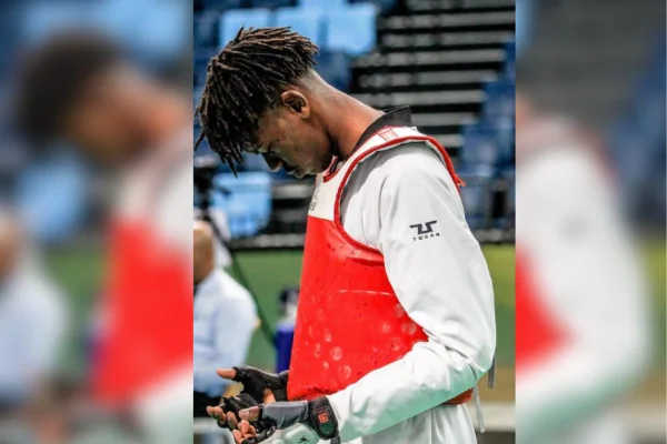 imagem colorida mostra atleta de taekwondo. ele é negro, está vestido com o uniforme do esporte e está olhando para suas mãos - metrópoles