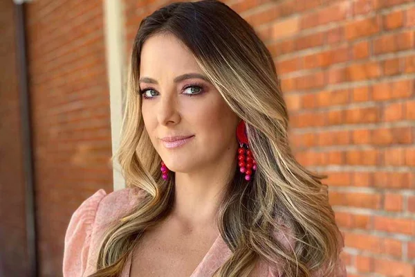 Foto colorida de Ticiane Pinheiro. Ela tem pele clara, cabelo loiro escuro, usa brinco vermelho e uma blusa rosa - Metrópoles