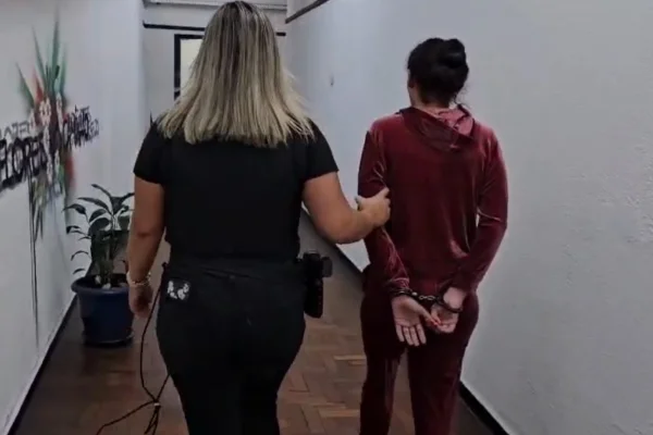 Imagem colorida de mulher presa sendo conduzida por delegada. Metrópoles