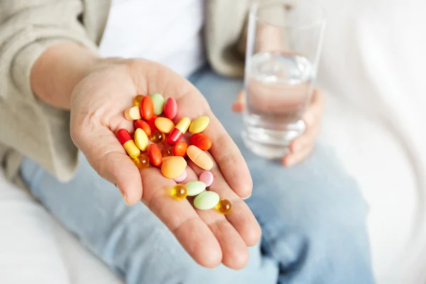 Close up das mãos de uma pessoa segurando e mostrando vários medicamentos coloridos. Conceito de vitaminas. Metrópoles