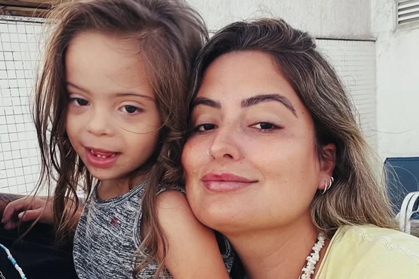 Foto colorida de Tatah Fávero e Dom, de 4 anos. Ela está com uma camisa amarela, colar, é branca e tem o cabelo claro. Ele tem o cabelo grande, é branco e usa uma roupa colorida - Metrópoles