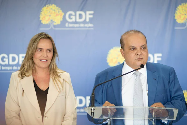 Fotografia colorida mostra homem e mulher com roupas formais discursando em evento