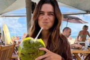 Mariana Goldfarb posa sorridente tomando água de coco