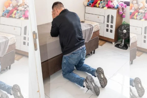 Homem ajoelhado com braços apoiados em cama rezando - Metrópoles