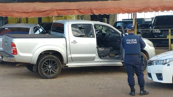 Caminhonete prata com marca de tiro em janela, porta aberta e policial militar