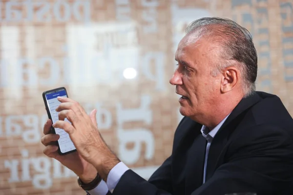 Homem segurando celular e apontando para tela do aparelho