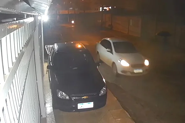 Carro branco em movimento passando em frente a casa