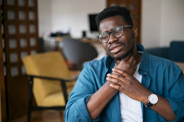 Homem adulto leva mãos ao pescoço por sentir dor aparentemente aguda
