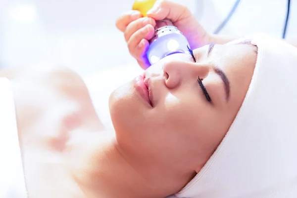 Young beautiful Asian woman getting lifting anti-aging, face massage and skincare by electroporation facial therapy aesthetic cosmetology.