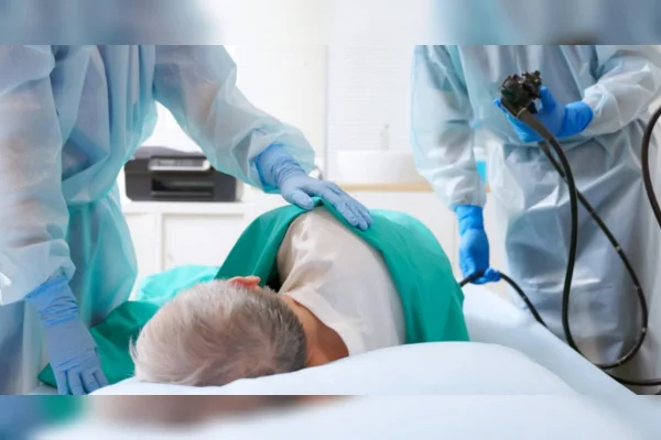 Um homem deitando com dois profissionais de saúde para iniciarem um exame colonoscopia