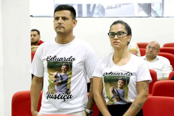 Imagem colorida de uma mulher e um homem vestidos com uma camiseta branca em homenagem ao filho que morreu por erro médico - Metrópoles