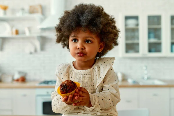 Foto colorida de bebê fofinha segurando bolinho doce com as mão e a boca suja de chocolate - Metrópoles