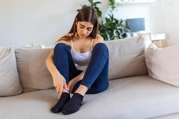 Mulher com meias sentada no sofá com semblante de dor