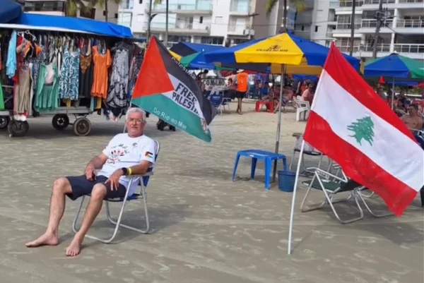 Imagem colorida de homem na praia com bandeira da Palestina e do Líbano