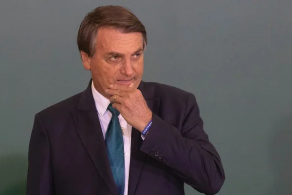 Bolsonaro durante cerimônia do "Brasil para Todos" no Planalto. Ele leva a mão ao queixo, olhando para frente - Metrópoles