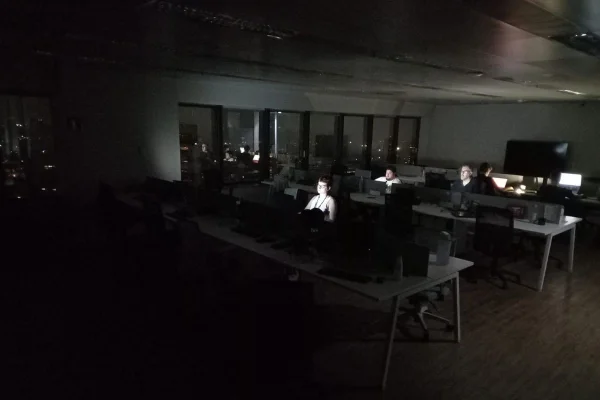 Imagens coloridas mostram escritório sem luz, com pessoas trabalhando apenas com a iluminação dos computadores