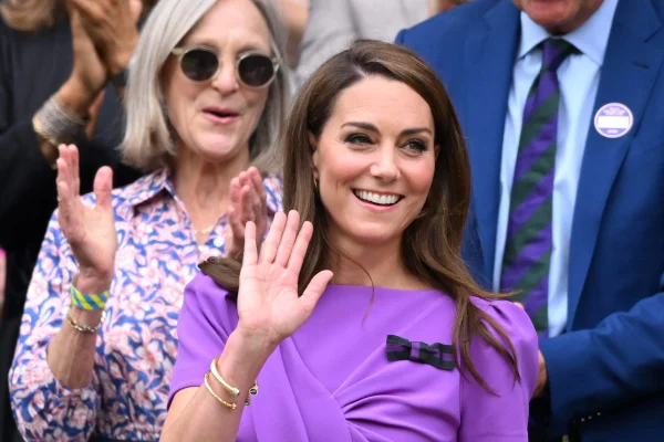 Foto colorida de mulher com vestido roxo. Ela está acenando - Metrópoles