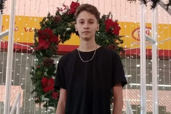 Imagem colorida de um jovem em frente a uma guirlanda de Natal