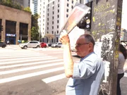 Pedestre se protege do sol com jornal em trecho da Avenida Paulista, em São Paulo
